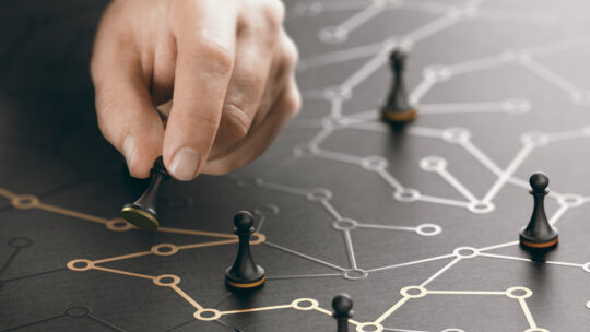 A hand moves a chess piece through a network grid with other pieces.