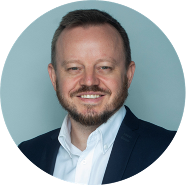 Headshot of Ashley Beattie, a smiling man with short dark hair, a beard and a navy suit.