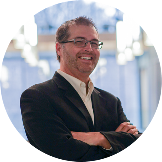 Headshot of Jan Klakurka, a smiling man with short brown hair, glasses and a black suit.