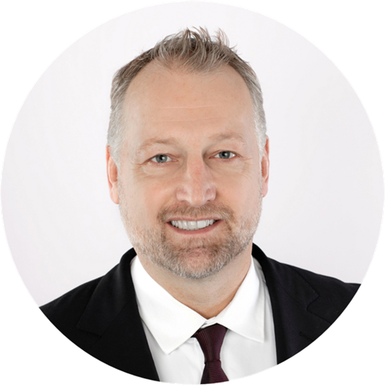 Headshot of Kirk Serjeantson, a smiling man with short greying hair, a beard and a black suit.