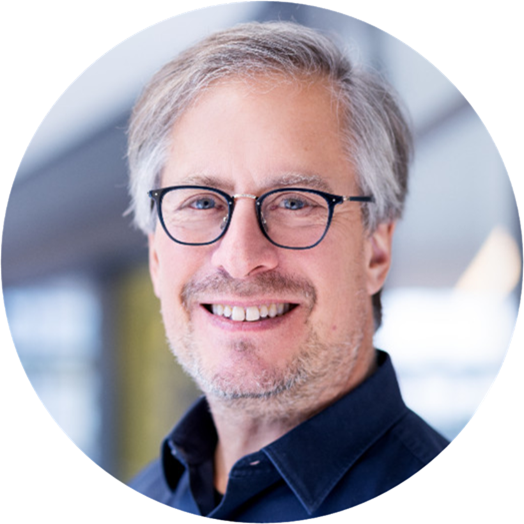 Headshot of Riel Miller, a smiling man with sliver hair, glasses, a beard and a navy dress shirt.